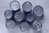 Nine sealed pull-tab cans photographed from directly above on a grey concrete surface.