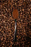 Roasted coffee beans filling the frame, with a worn metal spoon of fine ground coffee resting in the middle.